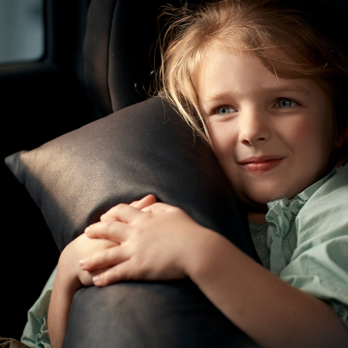 little girl smiling and holding her autonomy travel pillow sitting on the back seat of a car